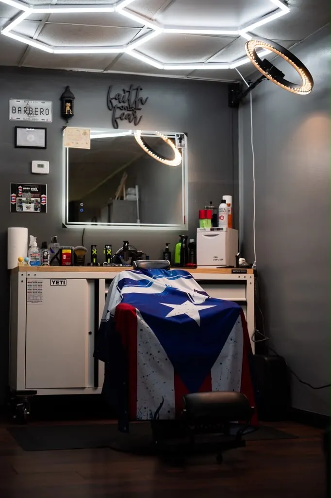 Barber chair with Puerto Rican flag cape under honeycomb lighting