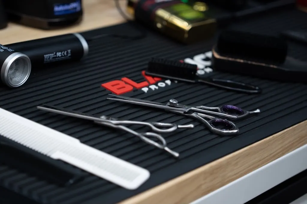 Professional barber shears, combs, and clippers laid out on a station mat